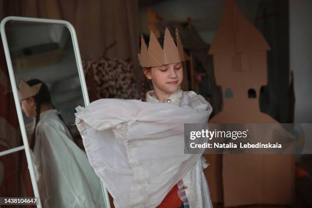 teenage girl dresses up in cardboard crown and white theatrical dress in front of mirror. school theatre and theatre production. - girl stage stock-fotos und bilder