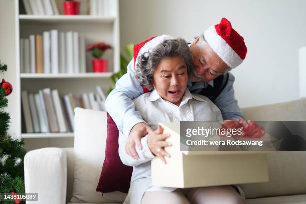elderly husband surprise giving christmas present with his wife - old man woman christmas stockfoto's en -beelden
