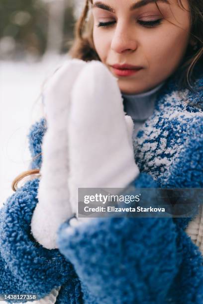 a frozen young woman in a warm fur coat warms her hands in knitted mittens in cold weather on a walk in the woods in winter outdoor - blue glove stock pictures, royalty-free photos & images