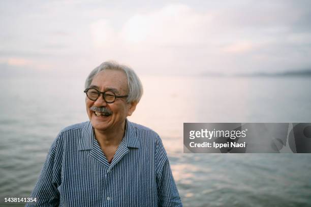 senior man laughing on beach at sunset - japanese ol stockfoto's en -beelden