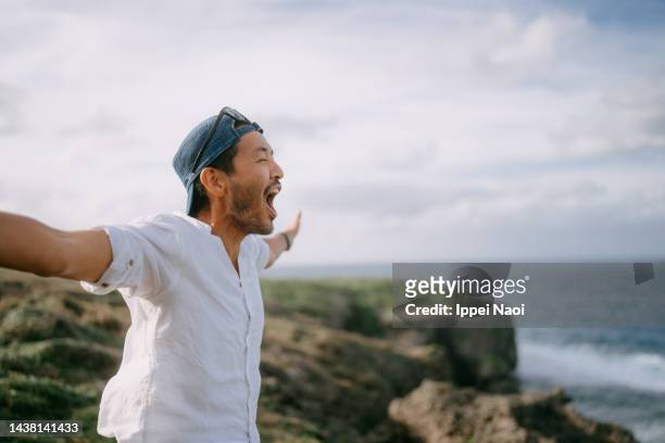 man shouting on top of cliff by sea - travel stock-fotos und bilder