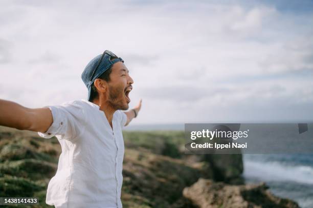 man shouting on top of cliff by sea - azië stockfoto's en -beelden