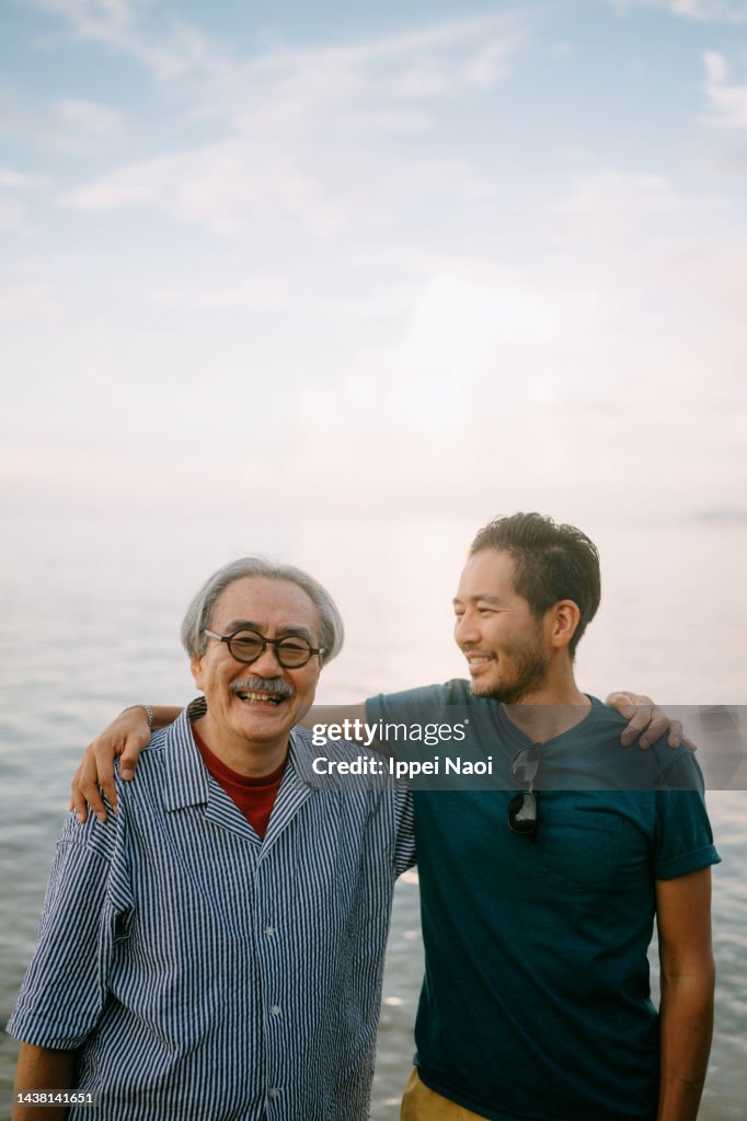 Senior father and adult son having fun on beach at sunset, Japan
