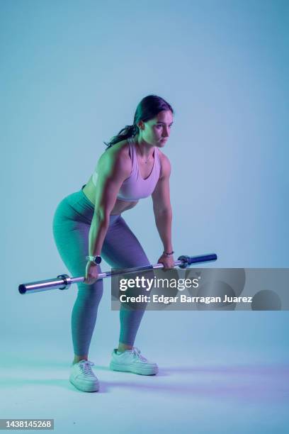 studio photo session of a young woman in sportswear doing rowing exercises, and a blue background - mexico training session stock pictures, royalty-free photos & images