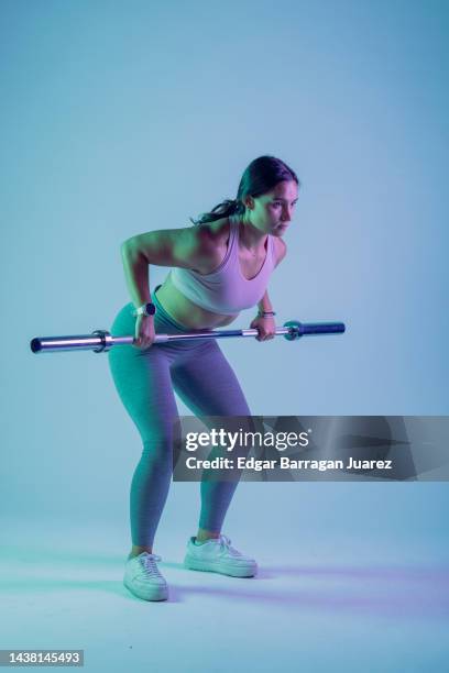 studio photo session of a young woman in sportswear doing rowing exercises, and a blue background - mexico training session stock pictures, royalty-free photos & images