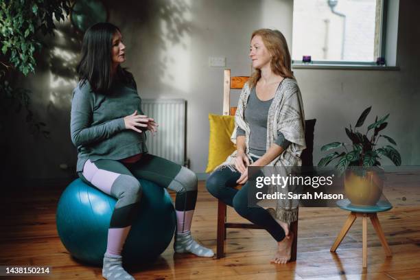 pregnant woman sat on birthing ball chatting to female yoga teacher - pregnant yoga stock-fotos und bilder