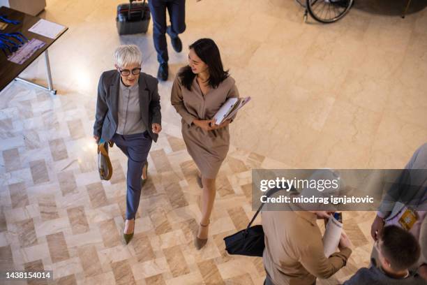 businesswoman entering a hotel with her assistant for a business conference - hotel hallway stock pictures, royalty-free photos & images