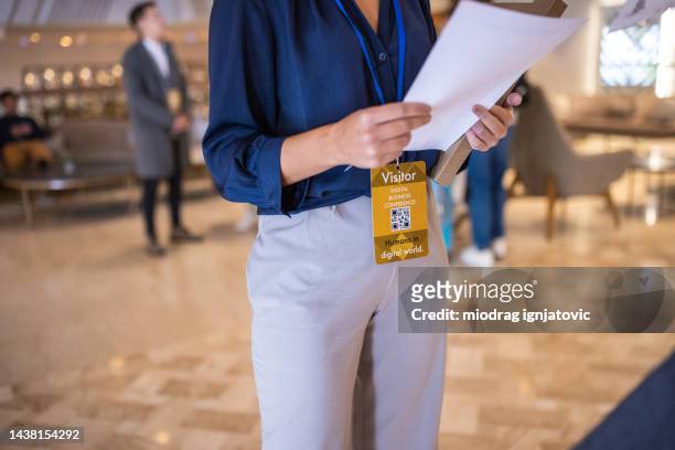 unrecognizable woman holding a document and wearing a business id card in a lobby - lanyard stockfoto's en -beelden