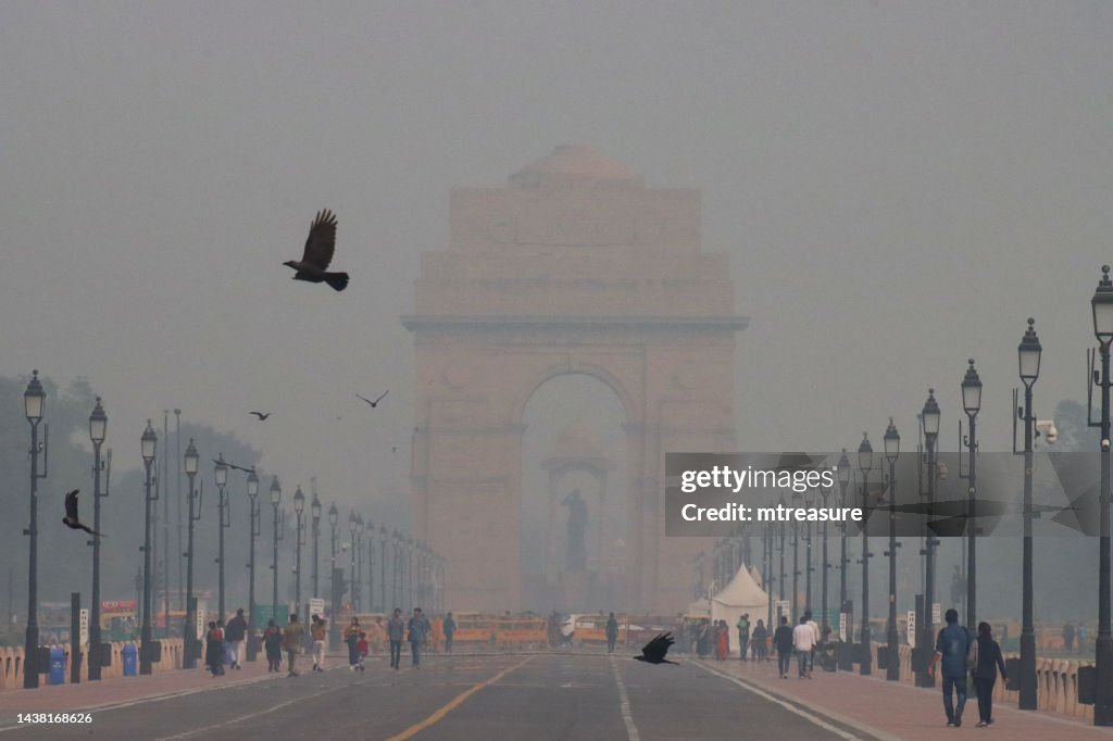 Imagen de All India War Memorial / New Delhi India Gate rodeado de contaminación nebulosa del cielo, multitudes de turistas en Kartavya Path (Rajpath), cielo brumoso y brumoso contaminado