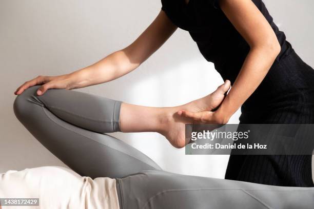 close up of unrecognisable female thai massage therapist stretching hip of female client. - druckpunkt stock-fotos und bilder
