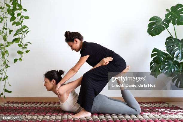 female latina thai massage therapist sitting on client feet to assist chest opening, stretching shoulders. - shiatsu stock pictures, royalty-free photos & images