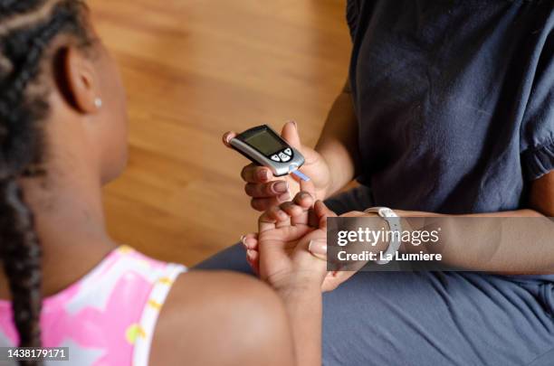 mother measuring daughter's glucose with digital device. - suiker stockfoto's en -beelden