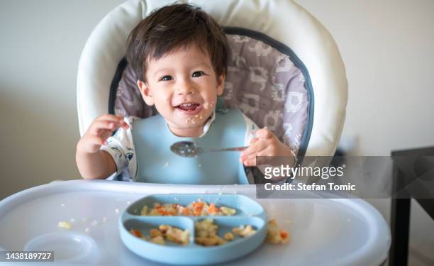 15 months old baby boy eating by himself using the spoon at home - asian baby eating stock pictures, royalty-free photos & images