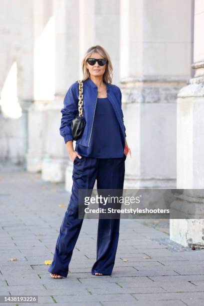 Influencer Gitta Banko wearing a blue shirt by Madeleine, a blue bomber jacket by Madeleine, blue wide leg pants by Madeleine, black high heel...