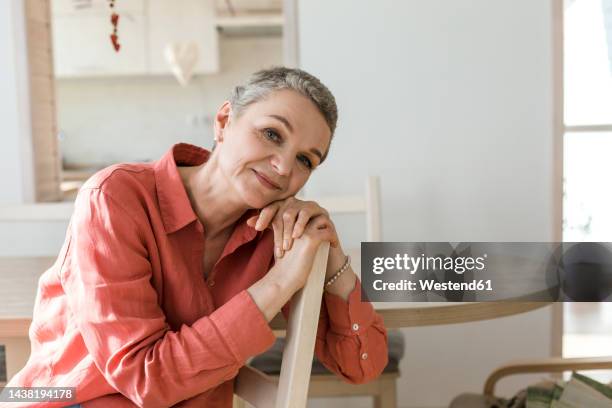 portrait of relaxed mature woman leaning on chair at home - une seule femme d'âge mûr photos et images de collection
