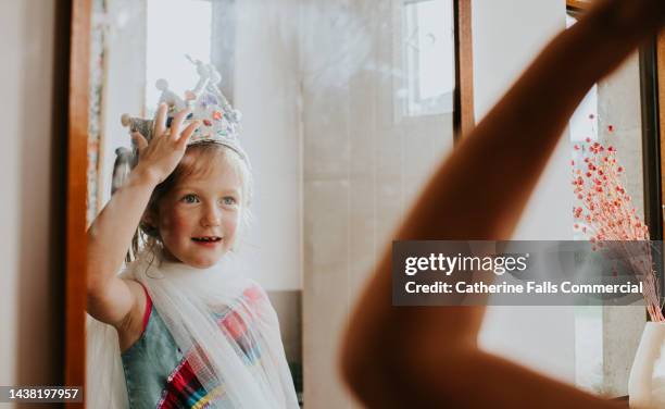 a cute little girl admires her homemade tin foil crown in a mirror - tin foil costume stockfoto's en -beelden