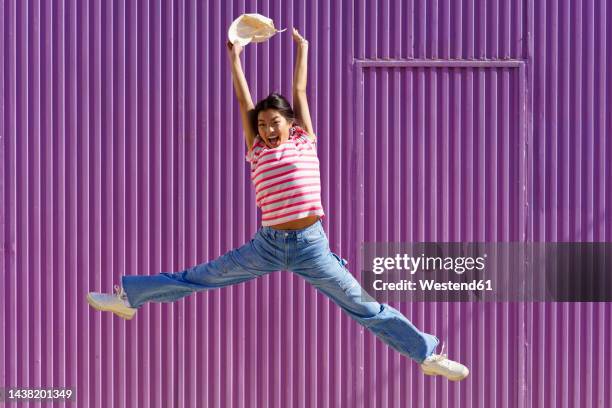 happy woman jumping in front of purple wall - legs spread woman stock pictures, royalty-free photos & images