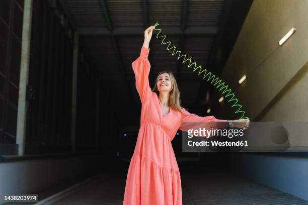 happy woman playing with metal coil toy on footpath - metal coil toy stockfoto's en -beelden