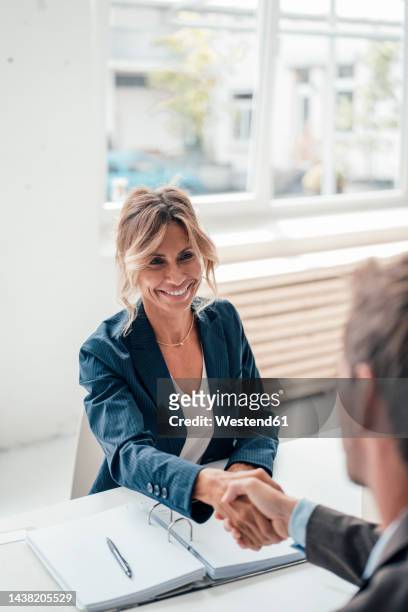 smiling businesswoman shaking hands with man at office - customer success stock pictures, royalty-free photos & images