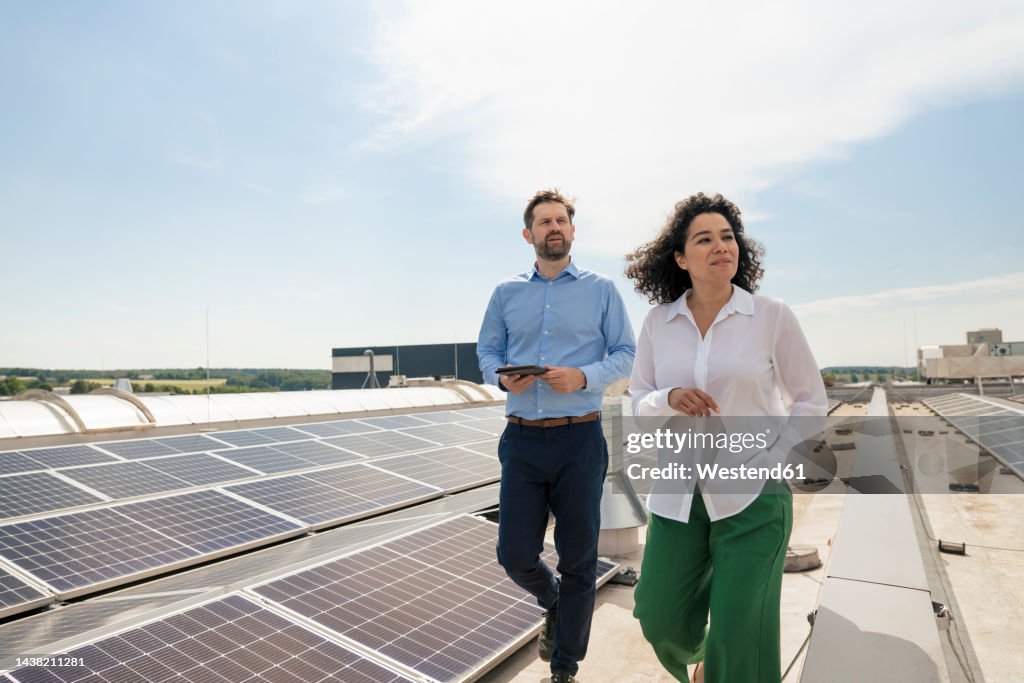 Businesswoman with businessman walking by solar panels on rooftop