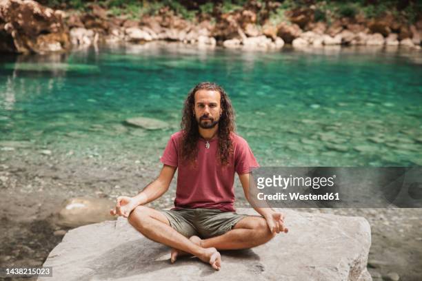 man with long hair doing yoga on rock in front of tara river - lotuspositie stockfoto's en -beelden