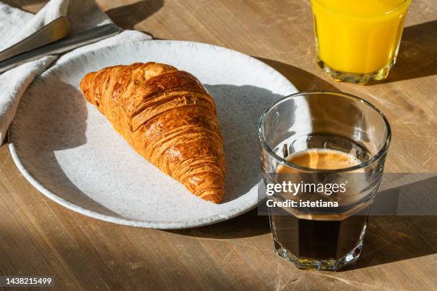 croissant, fresh coffee and orange juice on rustic table. sunlight with harsh shadows - croissant stock pictures, royalty-free photos & images