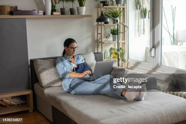 frau mit gebrochenem arm am laptop - gebrochener arm stock-fotos und bilder