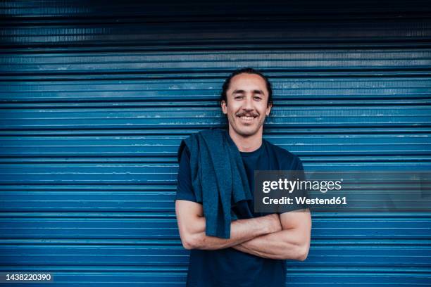 smiling young man with arms crossed in front of corrugated wall - roller shutter stock pictures, royalty-free photos & images