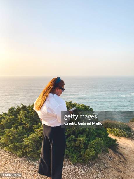 woman using her phone at cape espichel - distrikt setúbal stock-fotos und bilder