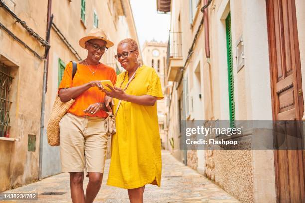 two mature women walking together exploring an old town in europe. - gay seniors stock pictures, royalty-free photos & images