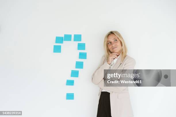 businesswoman standing next to question mark on the wall - mark think photos et images de collection