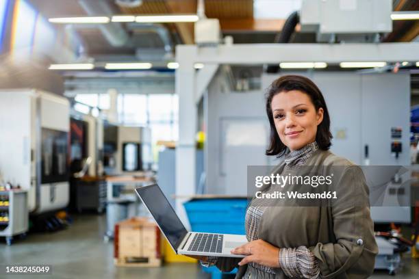smiling mature businesswoman holding laptop in industry - schweiz business stock-fotos und bilder