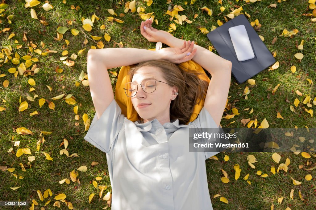Young woman lying down with eyes closed in autumn park