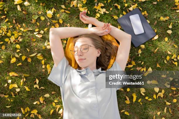 young woman lying down with eyes closed in autumn park - detox stock pictures, royalty-free photos & images