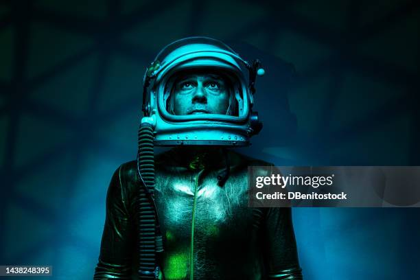 astronaut cosmonaut wearing a gold jumpsuit and helmet, in a green environment, looking up, with a mesh of light and green shadows in the background. exploration, space, planet, strange and alien. - science et technologie stock-fotos und bilder
