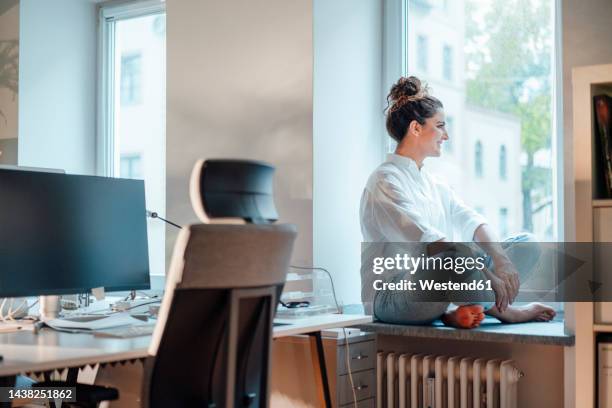 businesswoman looking through window in office - window seat stockfoto's en -beelden