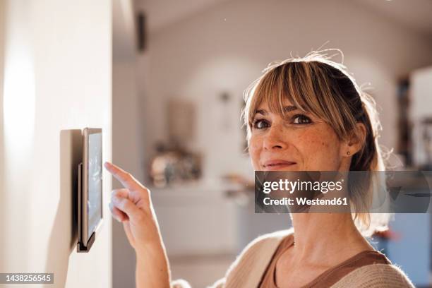 smiling woman using smart home app on tablet at home - home automation stock pictures, royalty-free photos & images