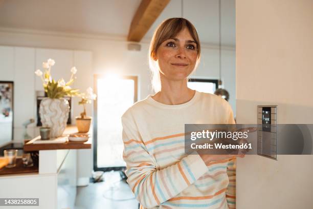 contemplative woman operating thermostat on wall at home - thermostaat stockfoto's en -beelden