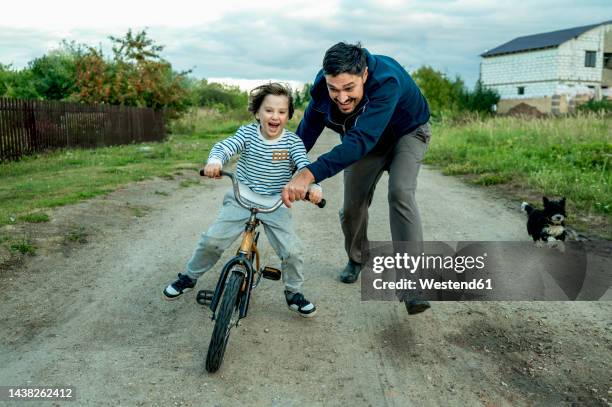 happy father teaching son to ride bicycle - riding stock-fotos und bilder