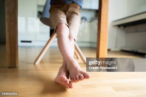 boy with legs crossed at ankle sitting on chair - barefoot floor stock pictures, royalty-free photos & images