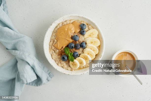 oatmeal porridge with peanut butter, blueberry, cinnamon, banana. traditional bunting breakfast served in ceramic bowl on gray background. top view. vegetarian and nutritious vitamin morning eating. classic hot homemade dietary meal - peanut butter stock pictures, royalty-free photos & images