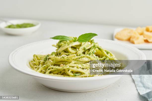 traditional italian pesto pasta spaghetti with pine nuts, garlic, basil, parmesan cheese. light gray table. homemade italian cuisine. vegetarian green pasta. - basil stock-fotos und bilder