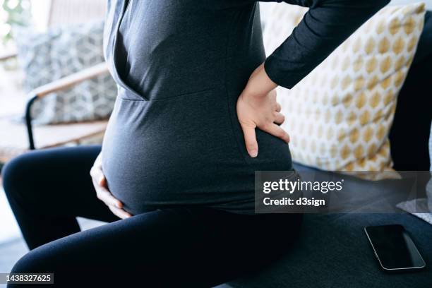 cropped shot, mid-section of pregnant woman touching her baby bump and lower back, suffering from backache. pregnancy health, wellness and wellbeing concept - morning sickness stockfoto's en -beelden