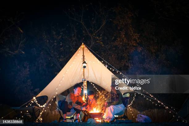 family sitting by camp fire at night - camping chairs couple stock pictures, royalty-free photos & images