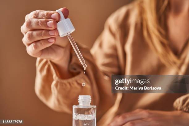 a girl in a beige dress holds a pipette with a drop of serum in her hands. - apothecary bottle stock pictures, royalty-free photos & images