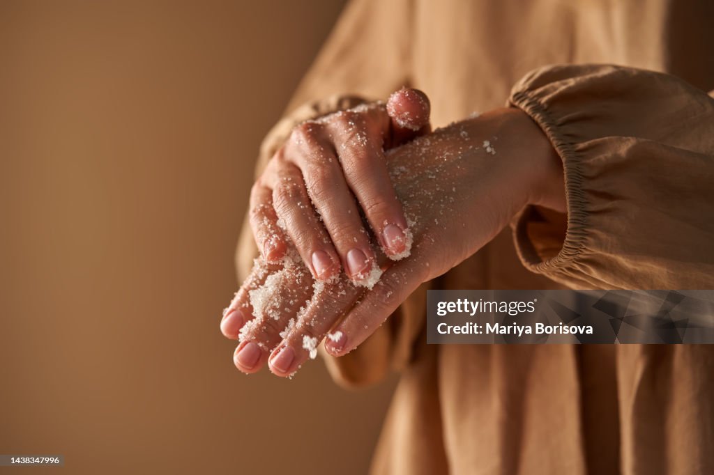 A girl in a beige dress rubs a natural sugar moisturizing scrub with her hand.
