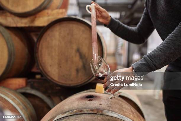 vin, cave et mains de l’homme avec pipette pour tester, déguster ou déguster un verre de vin rouge millésimé provenant d’un tonneau de stockage de bois. outils de l’industrie de l’alcool, inspection de contrôle de la qualité ou vérification  - cellier photos et images de collection