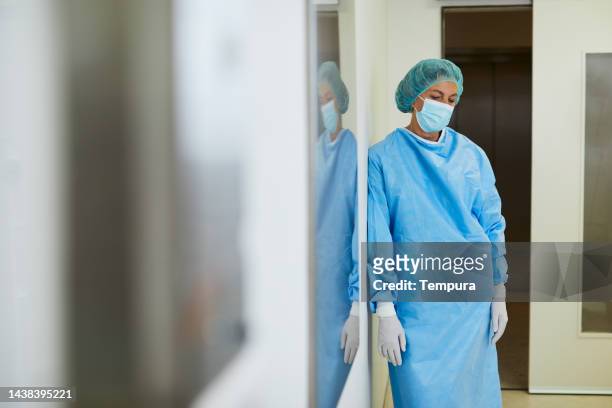 exhausted and sad operating room nurse in surgical clothing is resting on her feet after a long difficult operation - recovery position stock pictures, royalty-free photos & images