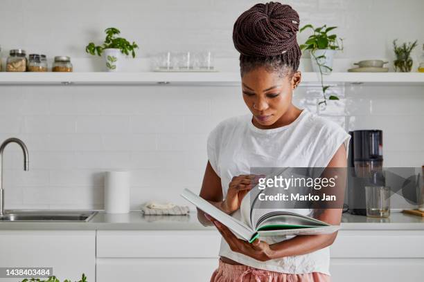 uma linda mulher na mesa da cozinha, lendo livro de receitas - cookbook - fotografias e filmes do acervo