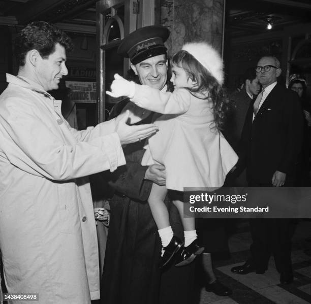 American singer and actor Eddie Fisher reaching for daughter Carrie Fisher who is being held by an usher at the Palladium Theatre in London on...